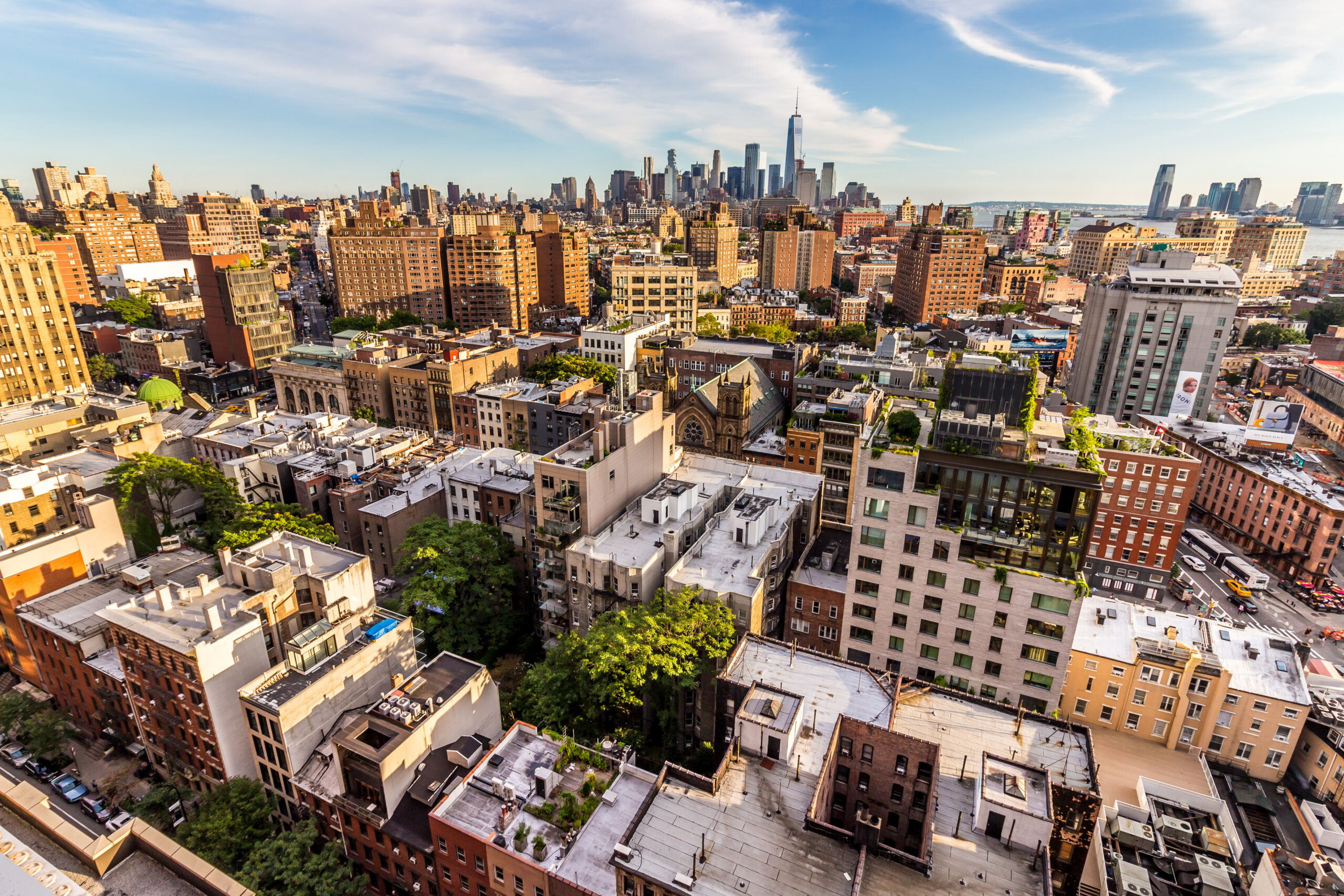 A springtime aerial view of Greenwich Village in Manhattan, showing bustling streets, residential buildings, and easy access to New York City transportation routes, highlighting the convenience of traveling to or from the neighborhood during the warmer season.