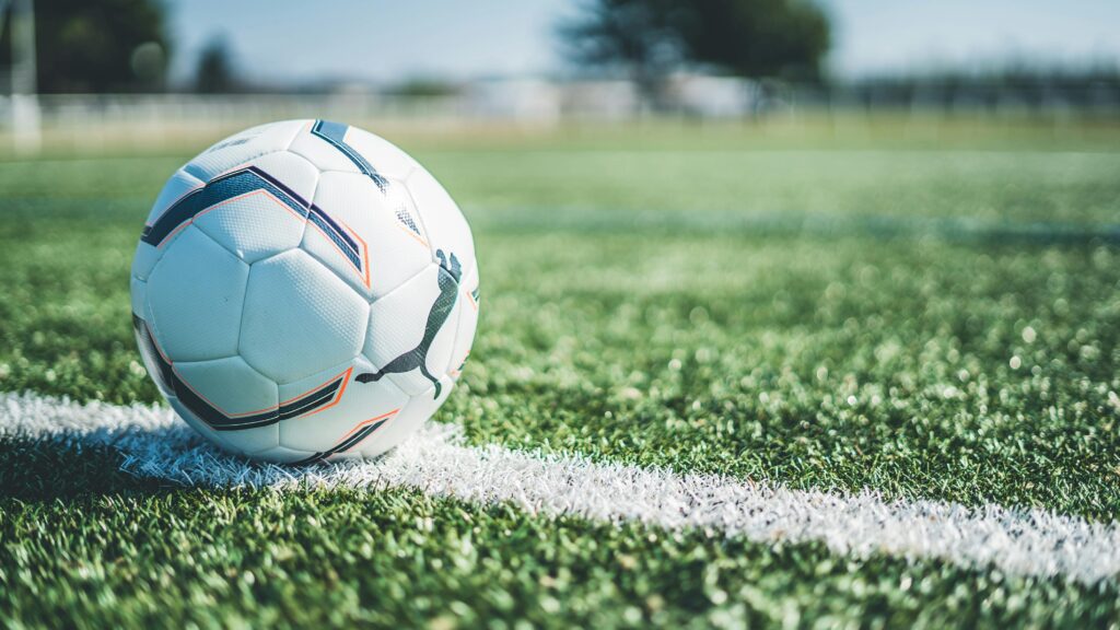 A football resting on the white touchline of a grass pitch on a sunny day — international football tournament New York New Jersey 2026